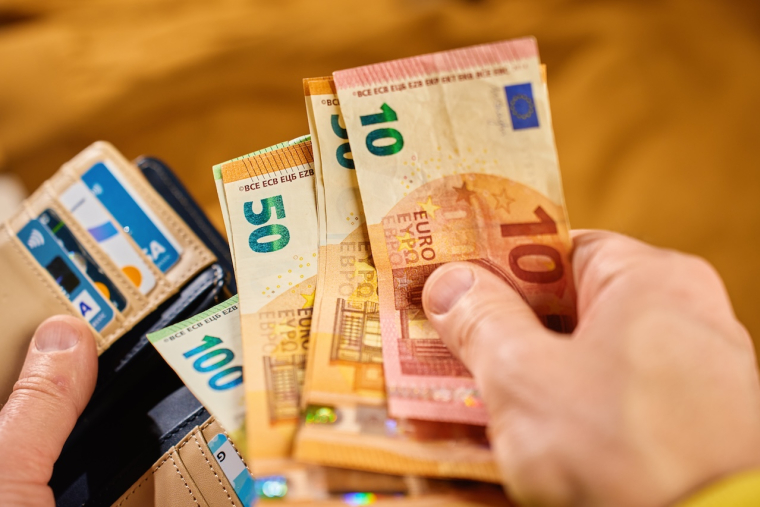 Personne tenant des billets et réfléchissant à une stratégie d'épargne.