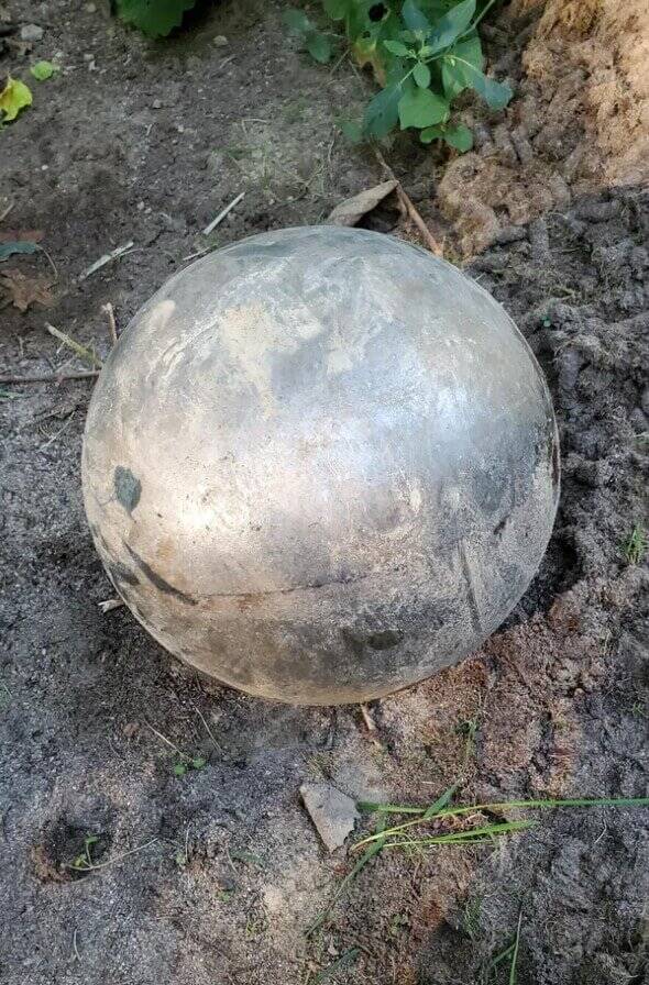Sphère en métal rouillée posée sur le sol en forêt