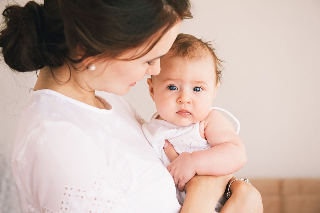 Père soutenant la mère qui tient enfin son bébé dans ses bras, regard complice.