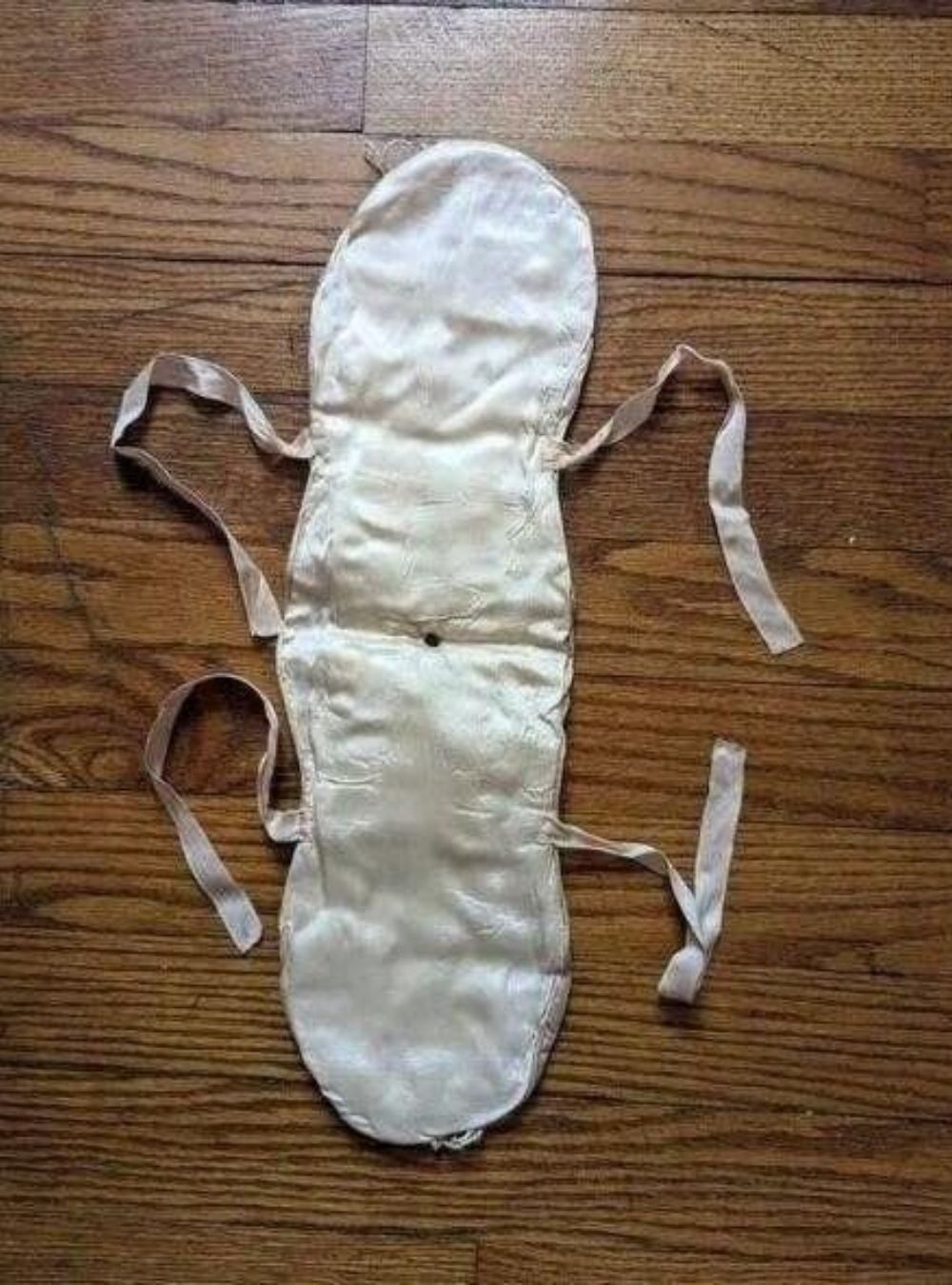 Photo d'un accessoire en tissu matelassé beige avec des nœuds sur les côtés, posé sur une surface en bois.