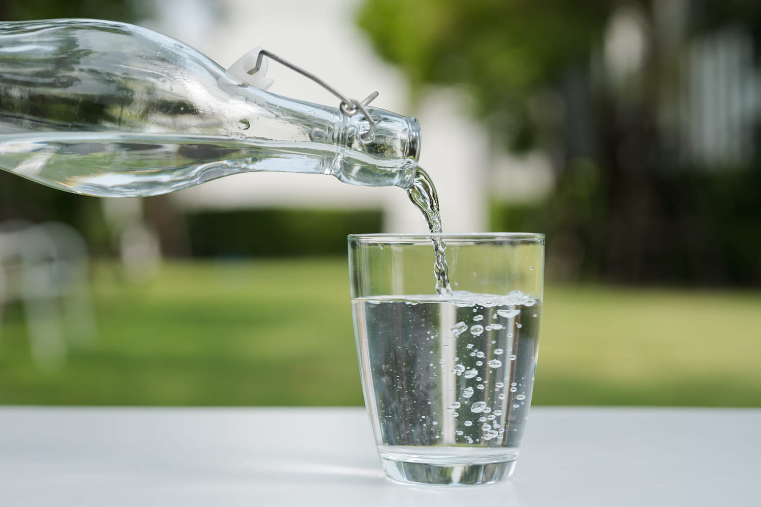 Femme buvant un verre d'eau à la lumière du jour, l'air sereine.