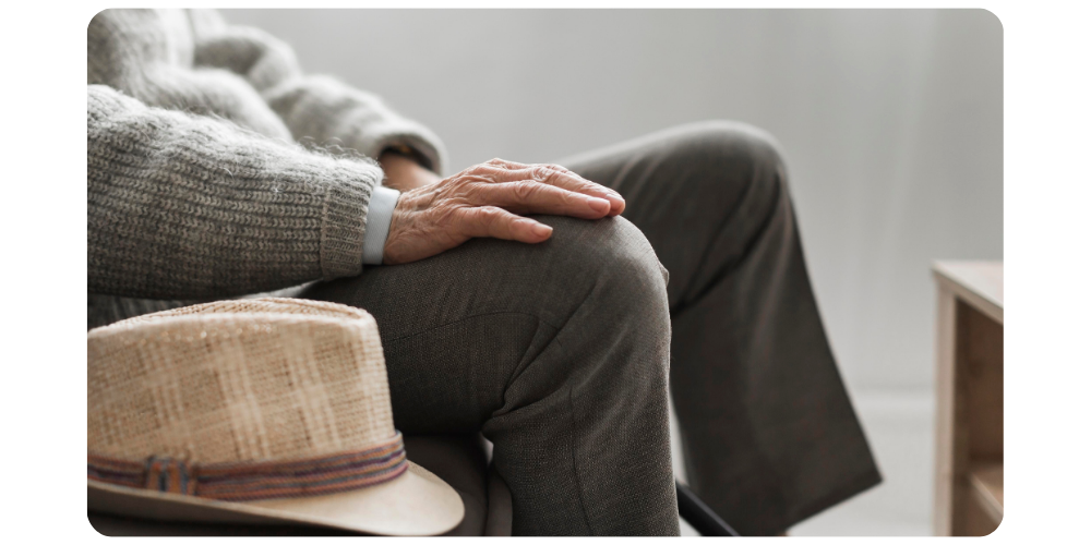 Une personne âgée souriante, tenant une tasse, regardant par la fenêtre d'une maison lumineuse