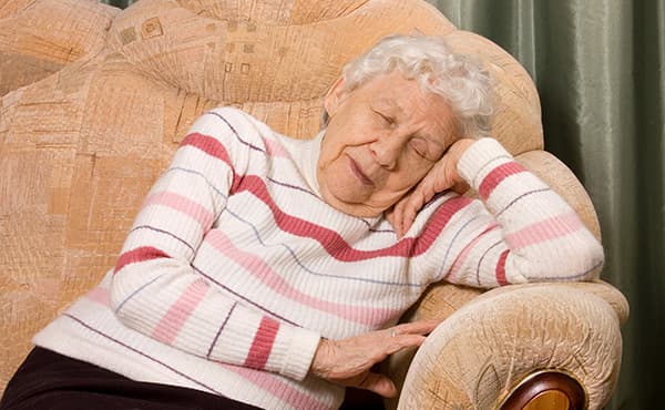 Une personne âgée est assise confortablement dans un fauteuil, illustrant un moment de calme et de bien-être.