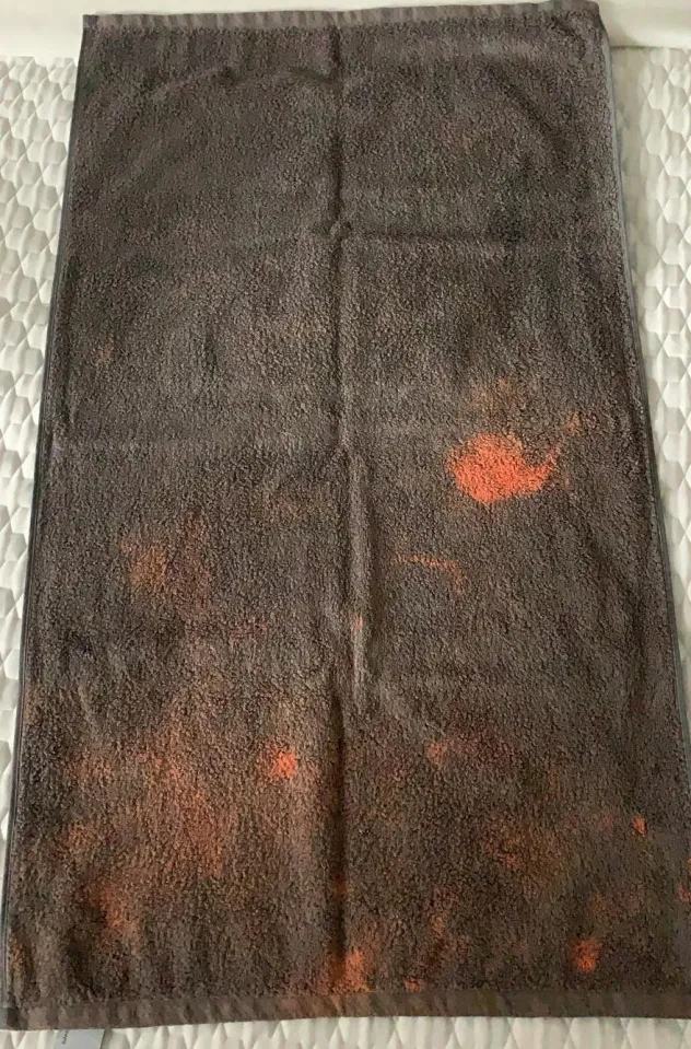 Détail d'une serviette de bain grise présentant une décoloration orangée