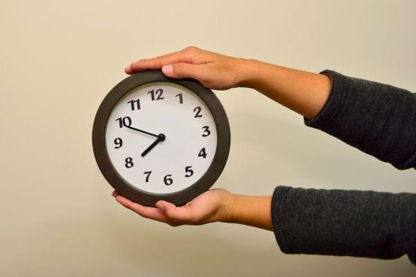 Deux mains tenant une horloge ronde noire.