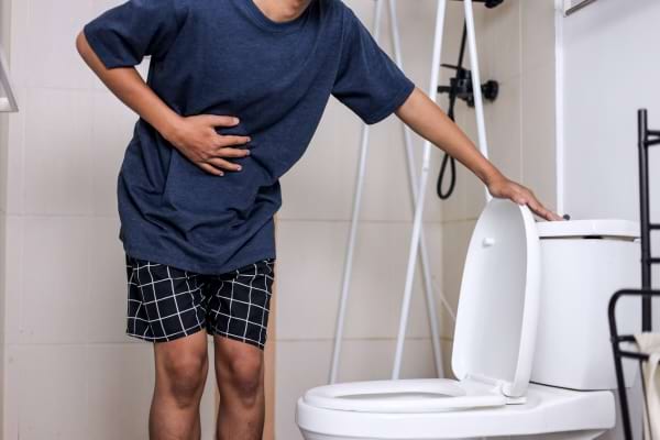 Muž ve spodním prádle si drží břicho poblíž toalety