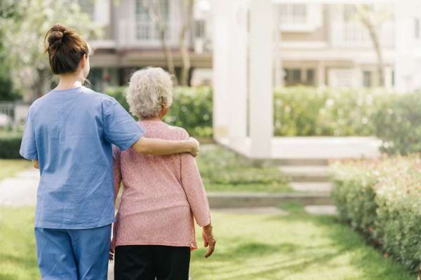 Une soignante accompagne une dame âgée en marchant dans un jardin.