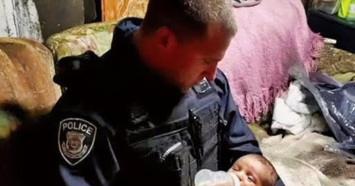 Un homme en uniforme de pompier tient délicatement un bébé emmitouflé dans sa veste, dans un environnement sombre et froid.