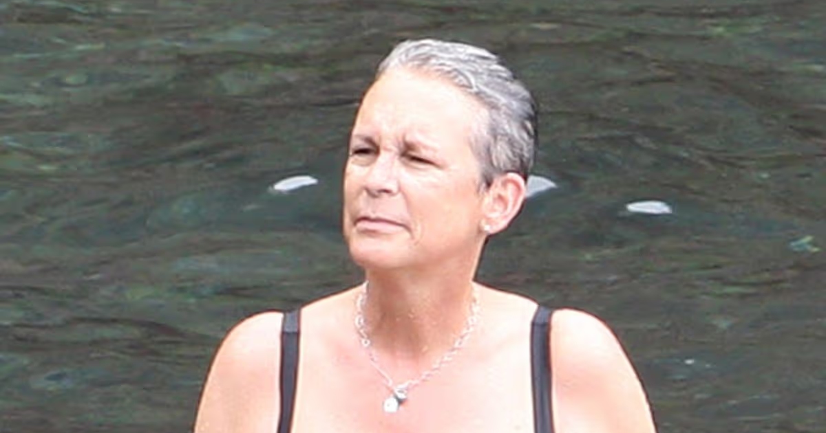 Jamie Lee Curtis souriante et détendue sur une plage, portant un maillot de bain noir