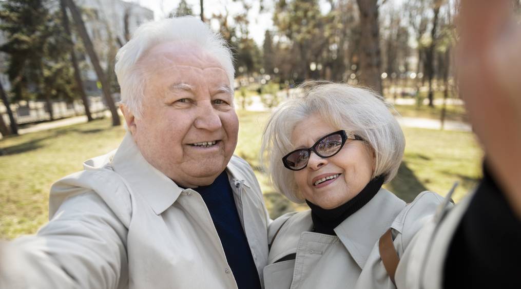 Un couple de personnes âgées souriantes, marchant main dans la main dans un parc ensoleillé