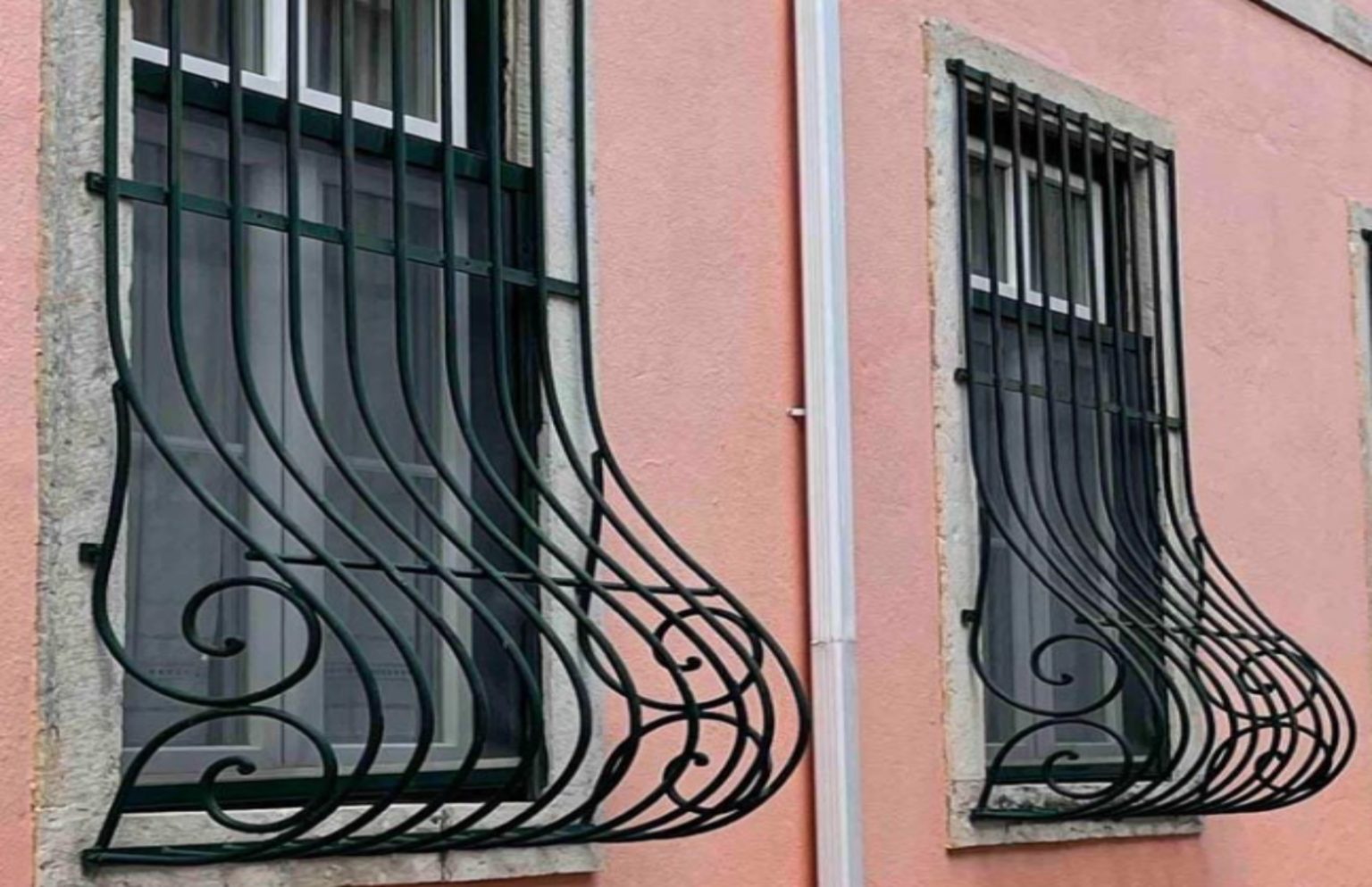 Détail d'une fenêtre équipée de barreaux au profil bombé, supportant des jardinières fleuries