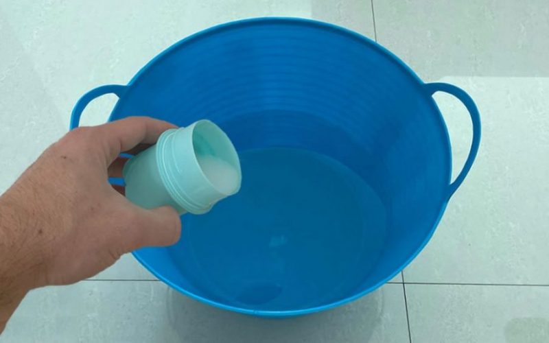 Préparation de la solution : une personne verse du vinaigre blanc dans un seau d'eau.