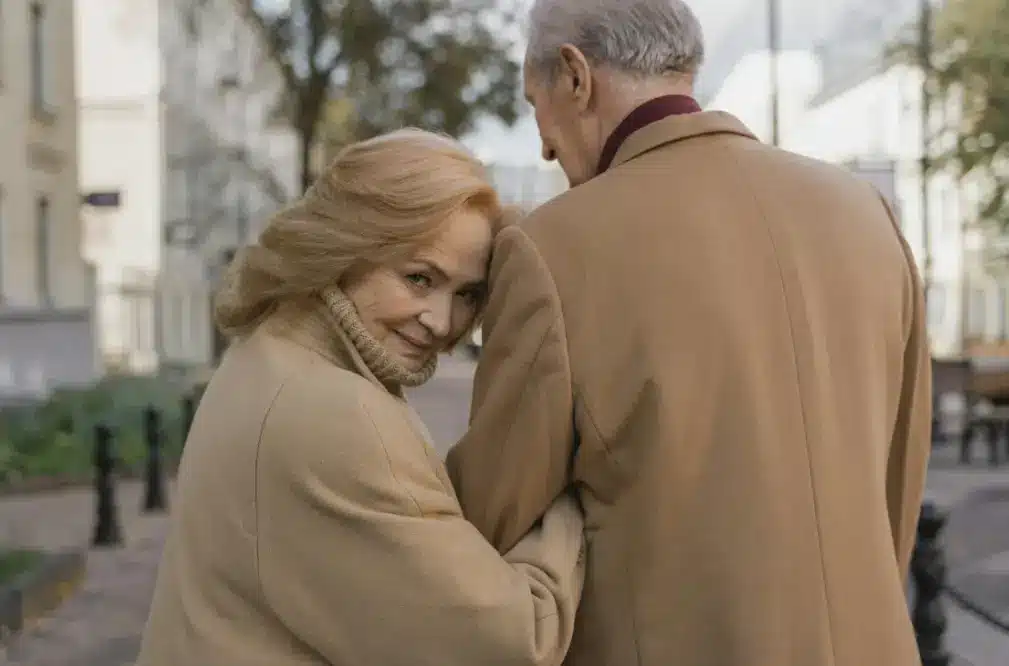 Un couple senior heureux se tenant la main et marchant ensemble dans un parc ensoleillé, symbolisant une relation complice.