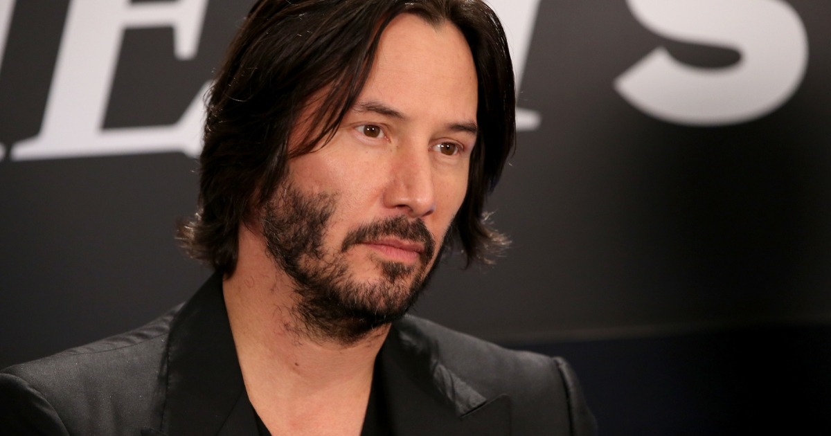 Keanu Reeves souriant simplement, vêtu de manière décontractée