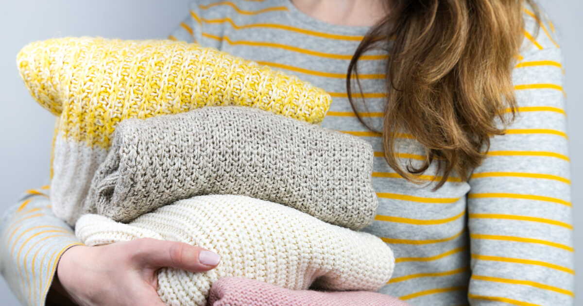 Jeune femme tenant des pulls chauds tricotés dans ses mains. Vêtements d'automne et d'hiver.