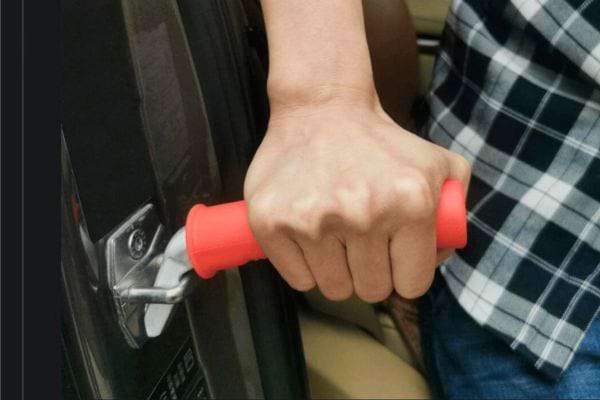 Personne tenant une poignée d'assistance rouge fixée sur une portière de voiture
