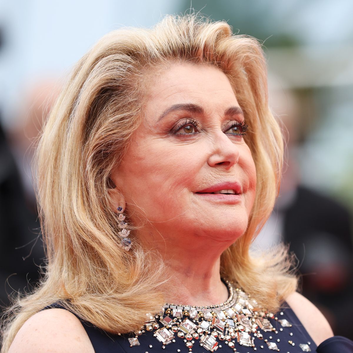 Catherine Deneuve souriante, avec une peau lumineuse, illustrant une beauté naturelle.